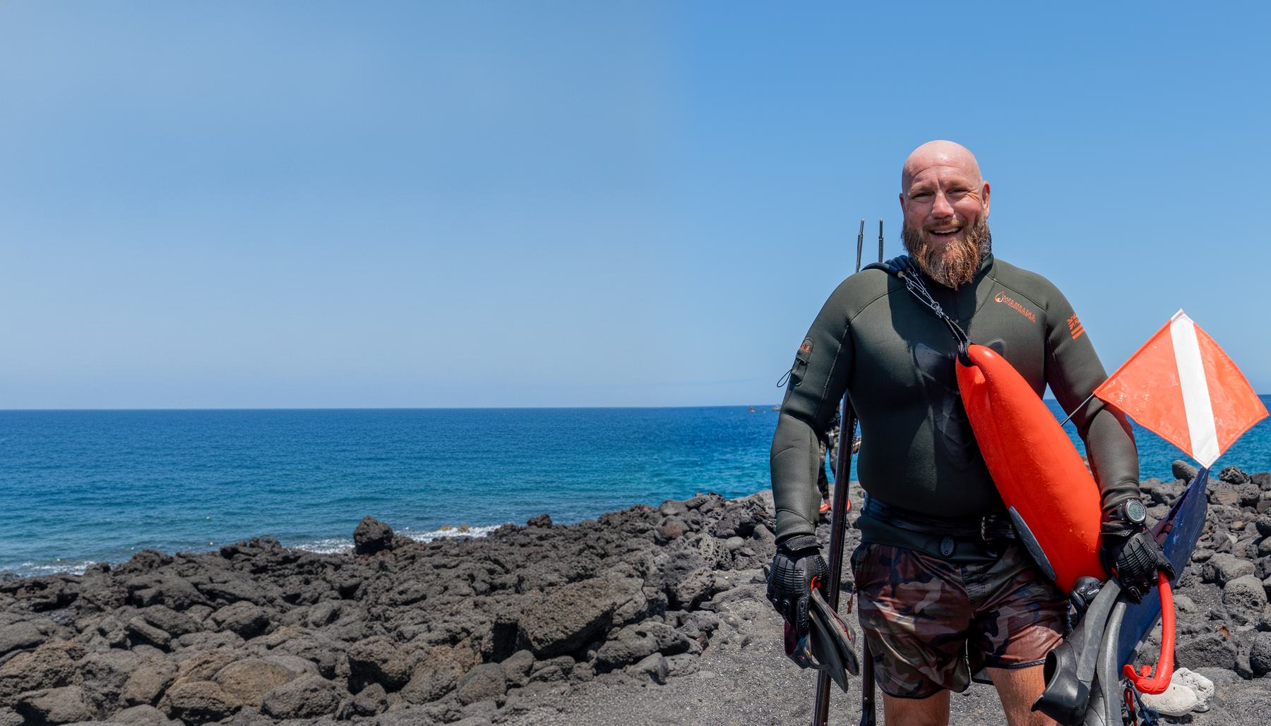 Bamm, Kona lead guide, grinning with dive float and speargun on the lava shoreline, Big Island of Hawaii